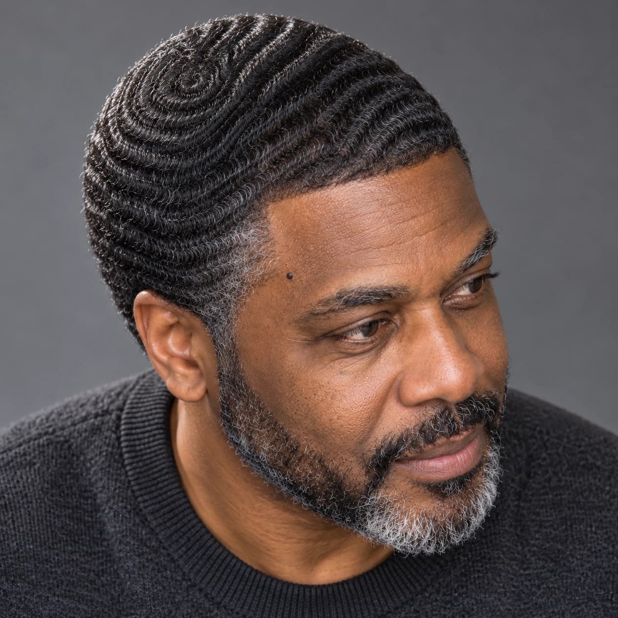 Man in his early 50s with a #1.5 low Caesar showing a defined 360 wave pattern and a soft line-up, high three-quarter view under raking light on a gray backdrop