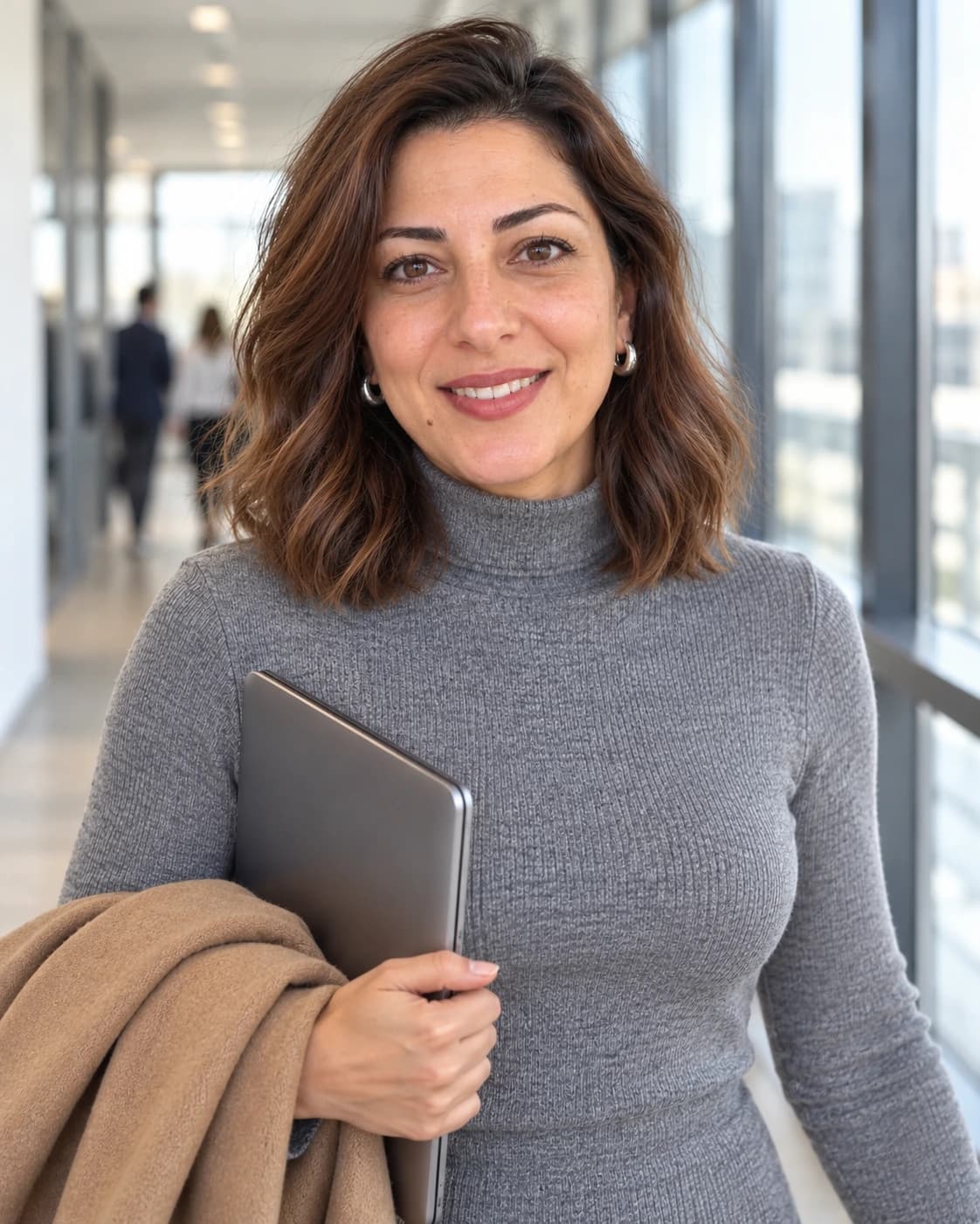 Woman in her early 40s with wavy hair cut to the collarbone with a soft bend, three-quarter view in a bright office corridor