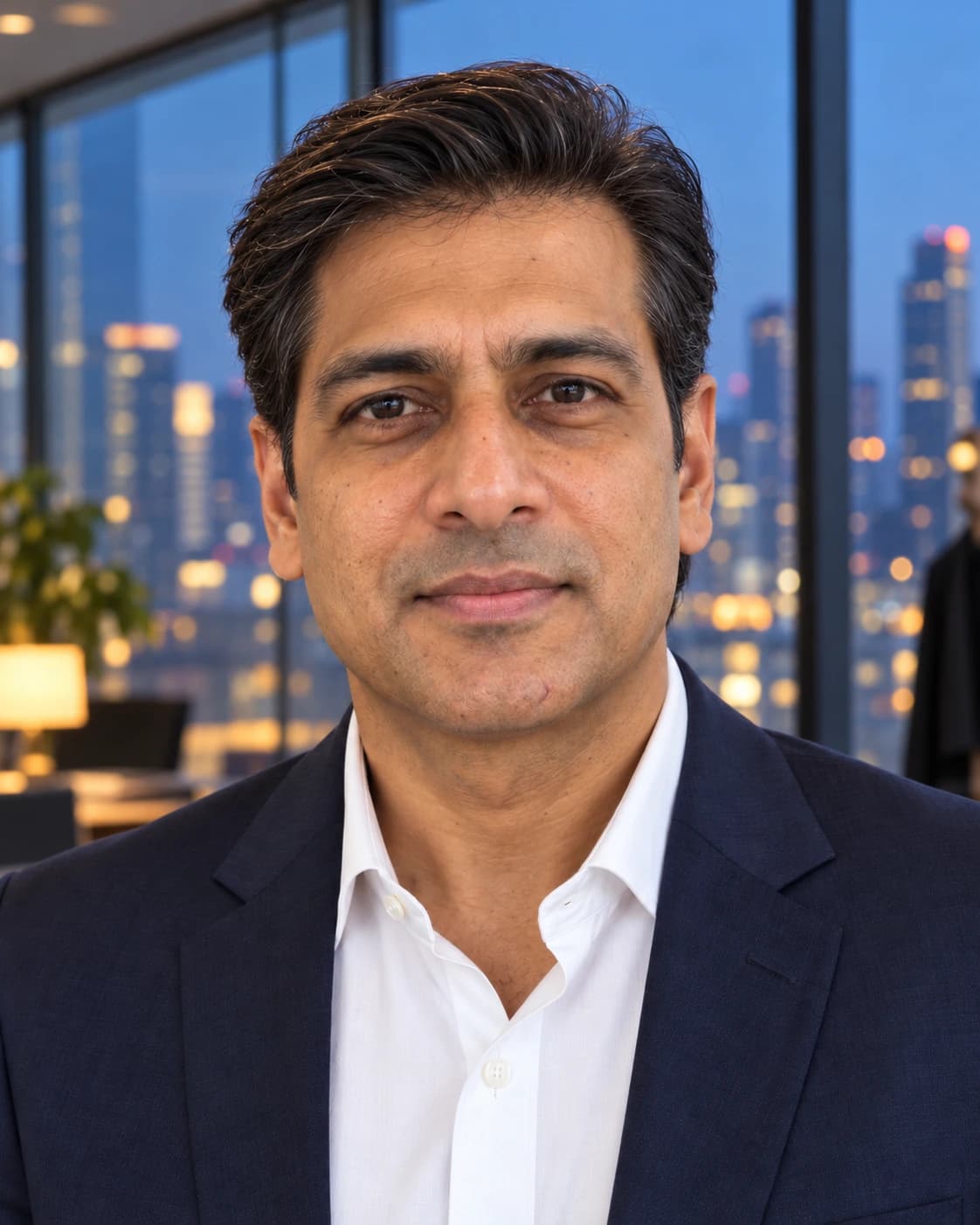 Man in his mid 40s with an executive contour, three inches of straight hair combed back with light hold over scissor-tapered sides, front view in a glass office at dusk